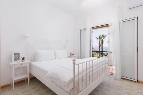 a white bedroom with a white bed and a window at The Island Life Apartments by Konnect, Ipsos Beach in Ýpsos