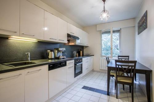une cuisine avec des armoires blanches et une table et des chaises dans l'établissement Le Bois Gentil - Grand appartement familial, proche de Genève et du Palexpo, à Saint-Julien-en-Genevois