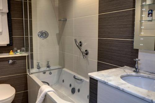 a white bath tub sitting next to a white sink at Ambleside Salutation Hotel & Spa, BW Premier Collection in Ambleside