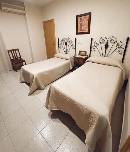 two beds in a room with white sheets at Hostal Restaurante El Paso in Bailén