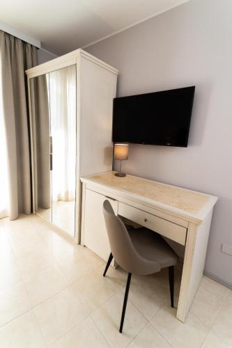 a desk with a television on a wall with a chair at Hotel Falli in Porto Cesareo