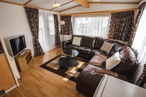 a living room with a leather couch and a tv at Lochlands 2br family caravan - pets-play park in Forfar