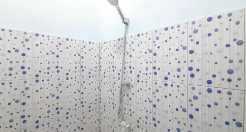 a shower in a bathroom with blue dots on the wall at Prima Homestay Mentawai Mitra RedDoorz in Tua Pejat