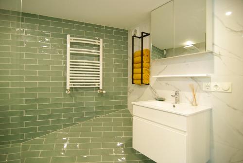 Un baño de azulejos verdes con lavabo y espejo. en Magnificent houseboat with a stunning view!, en Ámsterdam
