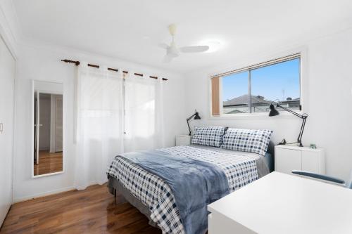 a white bedroom with a bed and a window at Close to lake, golf & beach, perfect for longer stays in Toukley