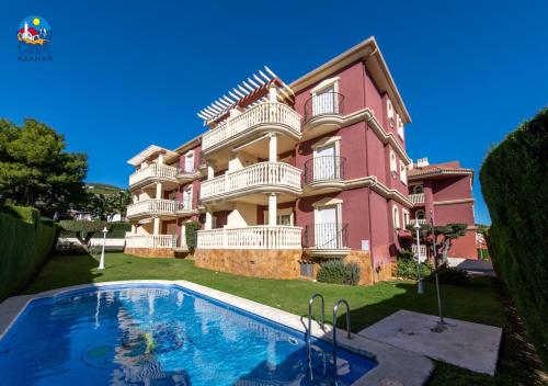 a large pink building with a swimming pool in front of it at Apartamentos Madeira Casa Azahar in Alcossebre