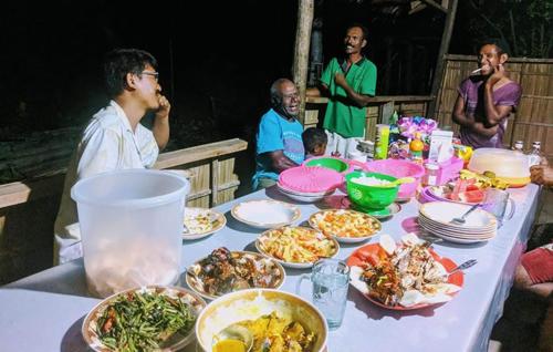 um grupo de pessoas sentadas à volta de uma mesa com comida em Gibran guest house em Kri