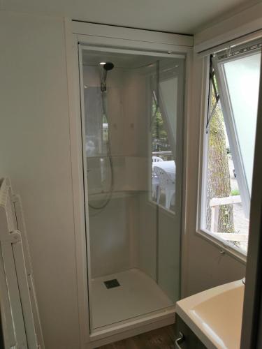La salle de bains est pourvue d'une douche en verre et d'une fenêtre. dans l'établissement mobilhome 29, à Pont-Aven