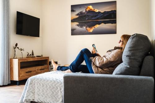 uma mulher sentada num sofá segurando um telemóvel em Apartamento Luxury en Bordes d'Envalira, Andorra em Soldeu