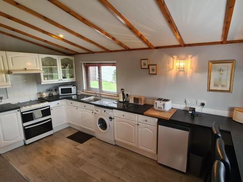 uma cozinha com armários brancos e uma máquina de lavar e lavatório em Hawthorn Self Catering Cottages em Benderloch