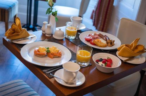 una mesa cubierta con platos de desayuno y zumo de naranja en Albany House en Penrith