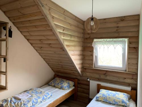 2 camas en una habitación con paredes de madera y ventana en Latarnia Wagabundy Bieszczady, en Wola Michowa