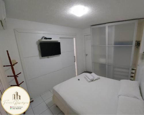 a small white bedroom with a bed and a television at American Flat - Ponta D'areia - Ferreira Hospedagens in São Luís