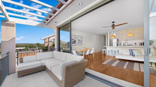 a living room with a white couch and a kitchen at Sea View - Ettalong Beach in Ettalong Beach