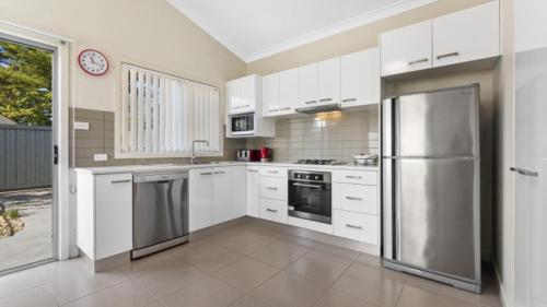 a kitchen with white cabinets and a stainless steel refrigerator at Ocean Sounds - Umina Beach in Umina