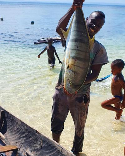 a man holding a fish on the beach at Hotel ECOLODGE LE RAVORAHA in Sainte Marie