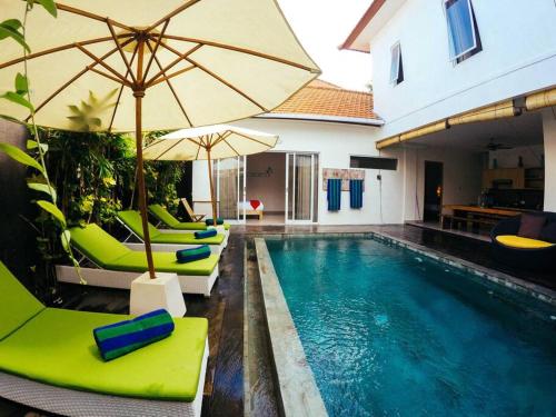 a swimming pool with green chairs and an umbrella at 3BR Del Mar Beach Villas Near La Plancha Seminyak in Seminyak