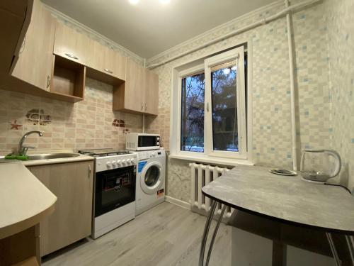 a kitchen with a stove and a sink and a washing machine at Квартира на Тулебаева in Almaty