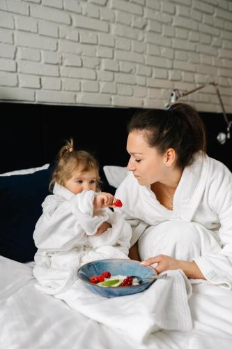 a woman and a child in bed with a plate of food at RATUSZOVA Stary Rynek Old Market PREMIUM Apartments & Restaurant AD 1954 in Poznań
