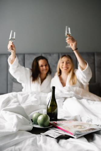 two women in bed holding up glasses of wine at RATUSZOVA Stary Rynek Old Market PREMIUM Apartments & Restaurant AD 1954 in Poznań