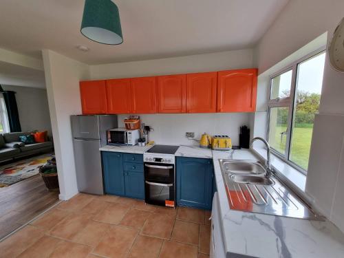 una cocina con armarios azules y naranjas y fregadero en Bungalow fully renovated 2022 close to slob lands and beach, en Ballygarrett