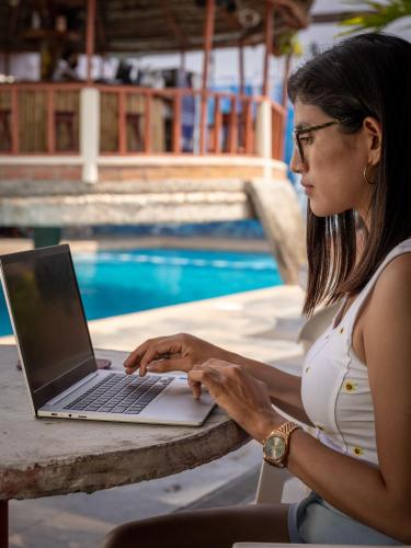 a woman sitting at a table with a laptop by a pool at Los Gavilanes Hotel in Pucallpa