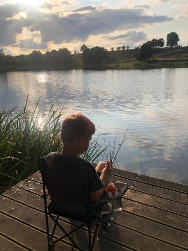 a boy sitting in a chair next to a lake at Domki Letniskowe Kalem in Zabin