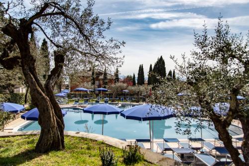 a swimming pool with blue umbrellas and chairs at Hotel Villa Paradiso in Passignano sul Trasimeno