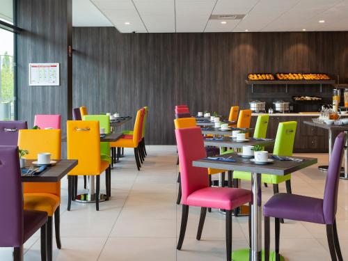une salle à manger avec des chaises et des tables colorées dans l'établissement Hôtel Roi Soleil Prestige Plaisir - St Quentin, à Plaisir