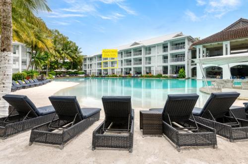 a swimming pool with chairs in front of a hotel at Beach Club Port Douglas Luxury Apartments in Port Douglas