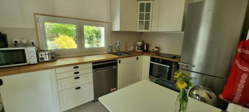 cocina con armarios blancos, fregadero y nevera en Jolie maison en pleine nature, en Villiers-sous-Grez