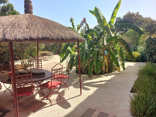 een patio met stoelen en een tafel en een rieten parasol bij Begue Pokai in Toubab Dialaw