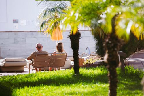 a man and woman sitting on a bench in the grass at Jacarandas Beach in Playa del Ingles