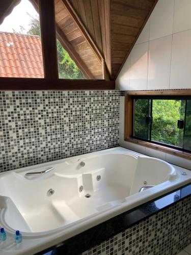 a large white tub in a bathroom with windows at Chales Elliotti in Monte Verde
