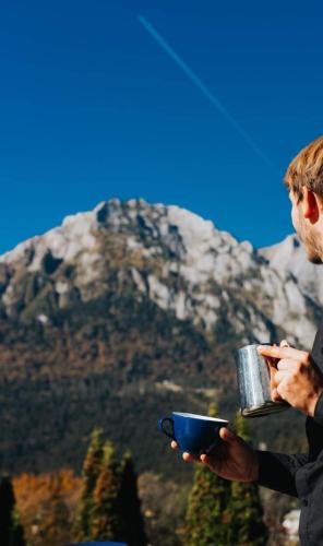a man holding a cup of coffee with a mountain in the background at Vila PANORAMIC Busteni in Buşteni