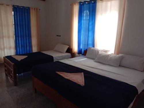 a bedroom with two beds and a window with blue curtains at Shivalaya Homestay in Madikeri