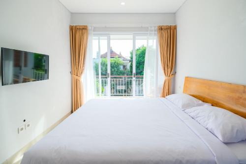 a bedroom with a large white bed and a window at Dharma Guest House Seminyak RedPartner in Seminyak