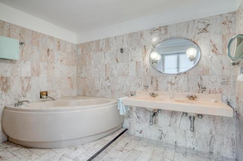 een badkamer met een bad, een wastafel en een spiegel bij Hotel Eisenhut in Rothenburg ob der Tauber