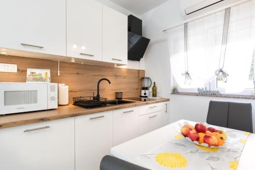 kuchnia z białymi szafkami i miską owoców na stole w obiekcie Apartman Ruza w Krku
