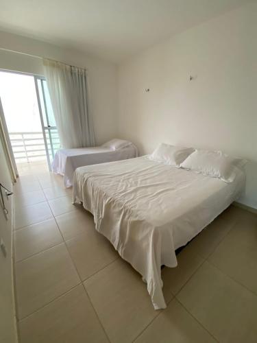 a white bedroom with two beds and a window at Casa em Condomínio, Aquiraz - CE in Aquiraz