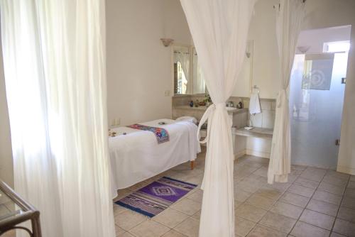 a white bedroom with a bed and a mirror at Hotel Hacienda Los Laureles in Oaxaca City