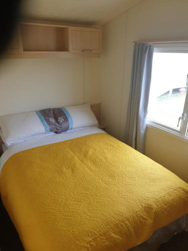 a bedroom with a yellow bed with a window at 4 BERTH CARAVAN SILVER BEACH INGOLDMELLS number 90 in Skegness