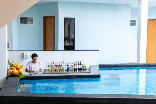 a man standing behind a bar next to a swimming pool at Coco & Pineapple Pants Hostel - CANGGU, BALI in Canggu