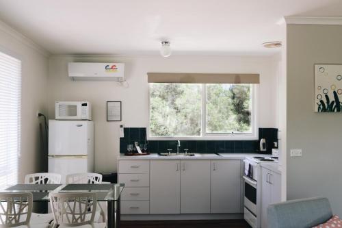 uma cozinha com armários brancos, uma mesa e uma janela em Bells Beach Cottages - Pet friendly cottage with wood heater em Torquay