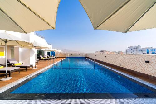 a swimming pool on the roof of a building with umbrellas at Centara Muscat Hotel Oman in Muscat