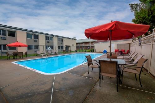 a pool with tables and chairs and a red umbrella at Red Roof Inn and Suites Herkimer in Herkimer