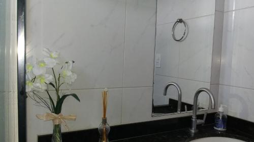 a bathroom sink with a mirror and flowers in a vase at Suíte INDIVIDUAL com Ar condicionado em AP Compartilhado in João Pessoa