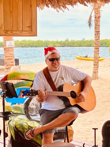 a man in a santa hat playing a guitar on the beach at Ocean Breeze in Placencia Village