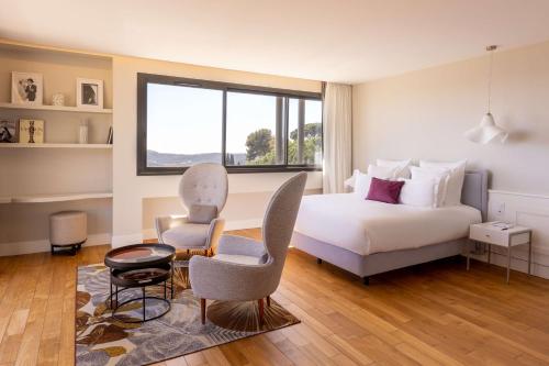 a bedroom with a bed and chairs and a window at Eden Rose Grand Hotel BW Premier Collection in Bormes-les-Mimosas