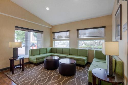 a living room with green couches and tables and windows at Comfort Suites DFW Airport in Irving